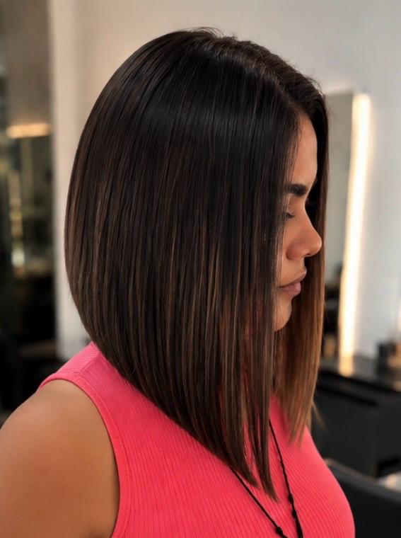 Corte bob invertido em ângulo acentuado, cabelo escuro com mechas finas, visto de perfil no salão.