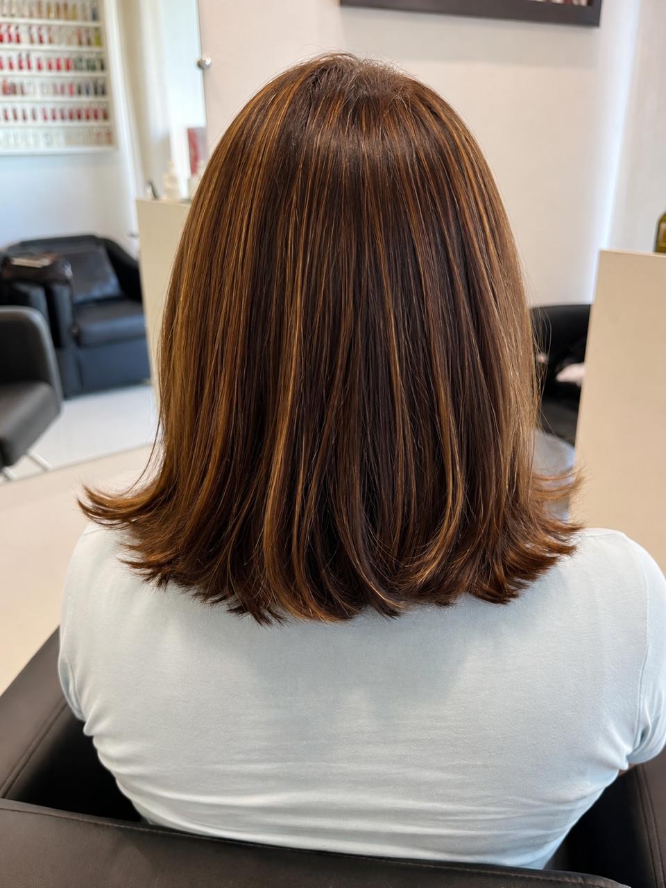 Corte bob reto na altura dos ombros com pontas para fora, base castanha com mechas caramelo, visto de costas no salão.